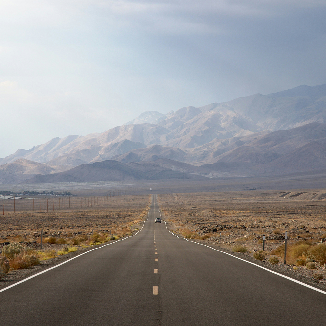On a cross-country road trip, a car drives toward the mountains in Southwest America.