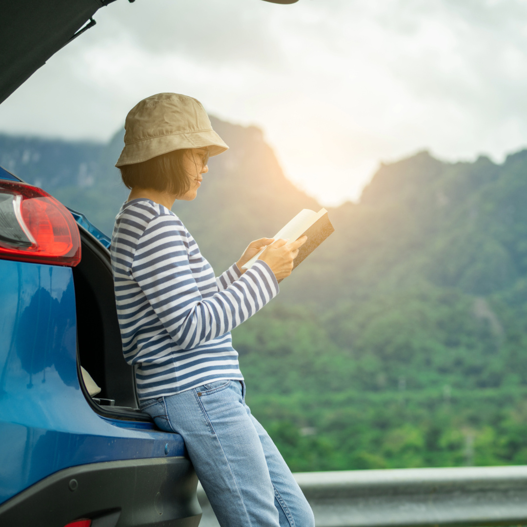 Person reading a book by their car during a digital detox vacation in a scenic mountain setting