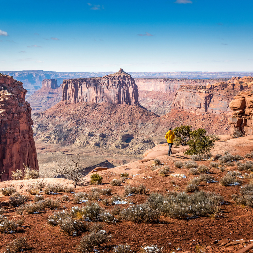 Hiker overlooking mesas and canyon cliffs at Island in the Sky Canyonlands under a clear blue sky