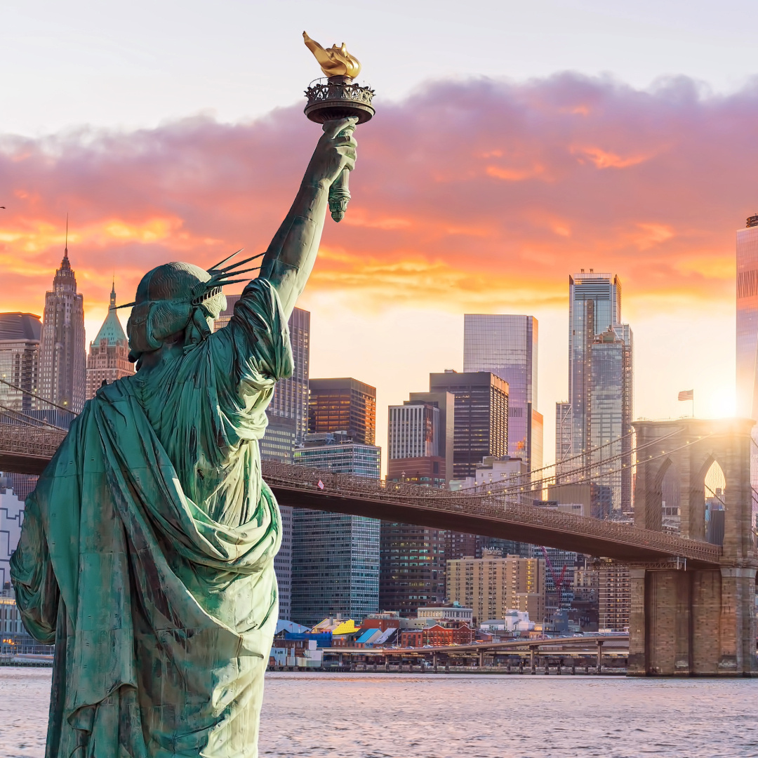 Statue of Liberty facing Manhattan skyline at sunset, symbolizing the most amazing cities in the U.S.