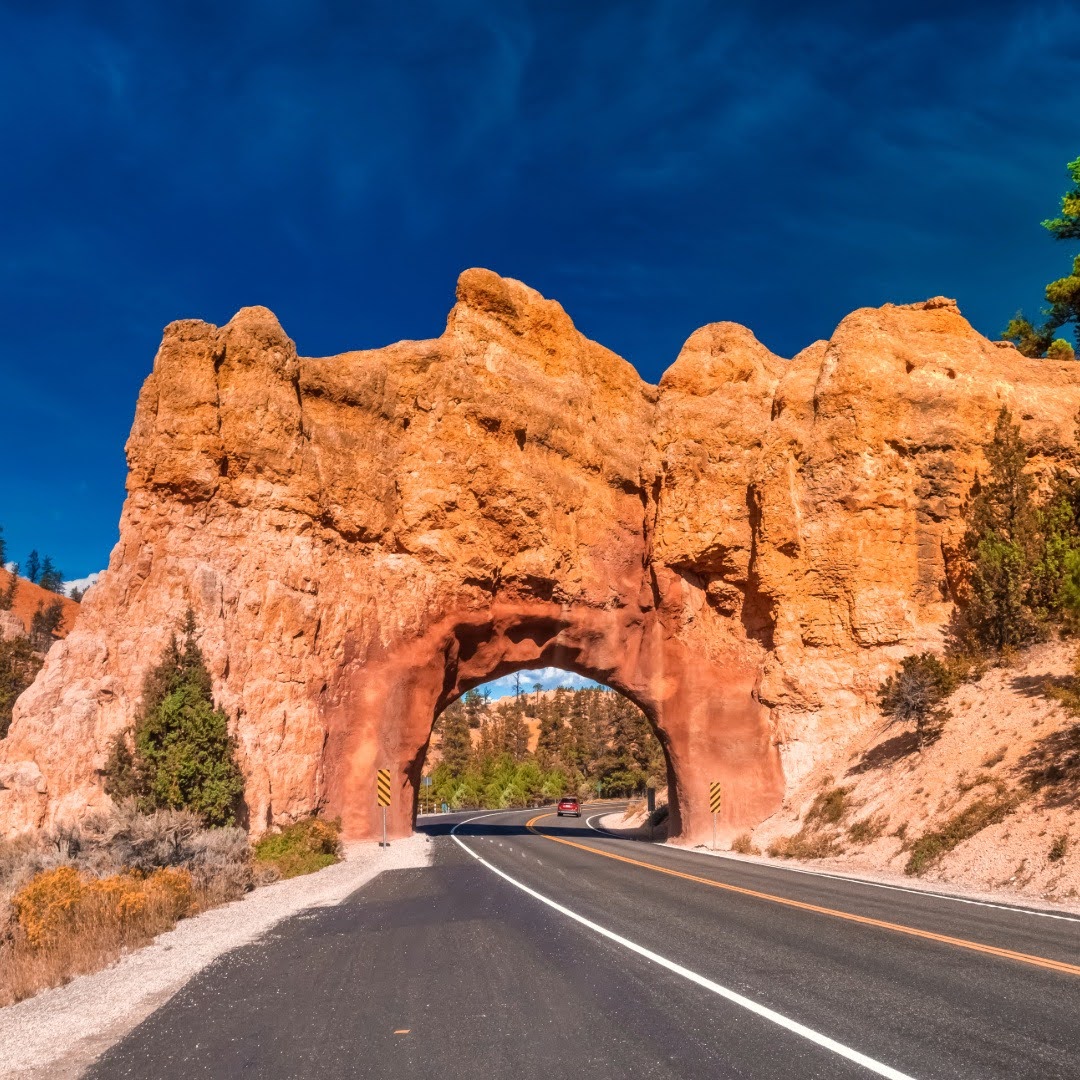Car driving through a red rock tunnel on a scenic highway, a classic view on national park road trips in the American Southwest.