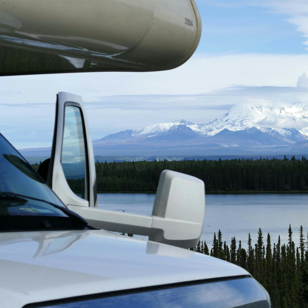 Close-up of an RV parked beside a lake by snow-capped mountains, inspiring RV road trip ideas for mountain adventures.