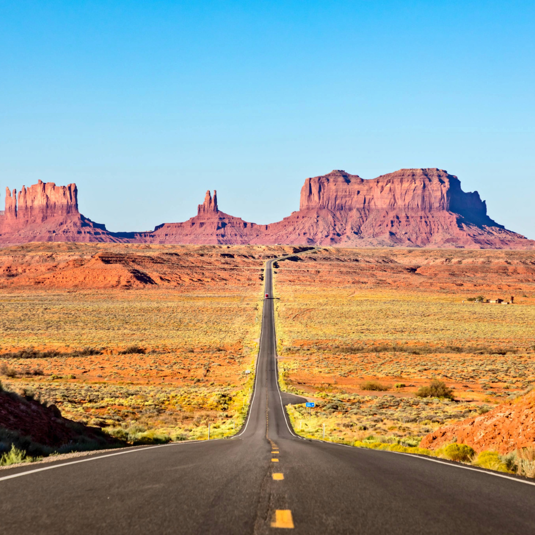 Open highway through red desert mesas under clear blue sky on a southwest road trip
